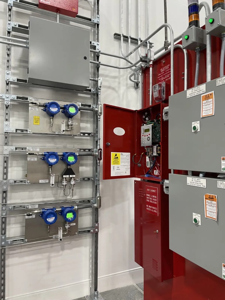 Electrical control panel and flow meters mounted on a wall, featuring various indicators and warning labels.