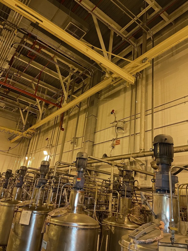 Interior of a manufacturing facility with large metal tanks and pipes, showcasing industrial equipment and infrastructure.