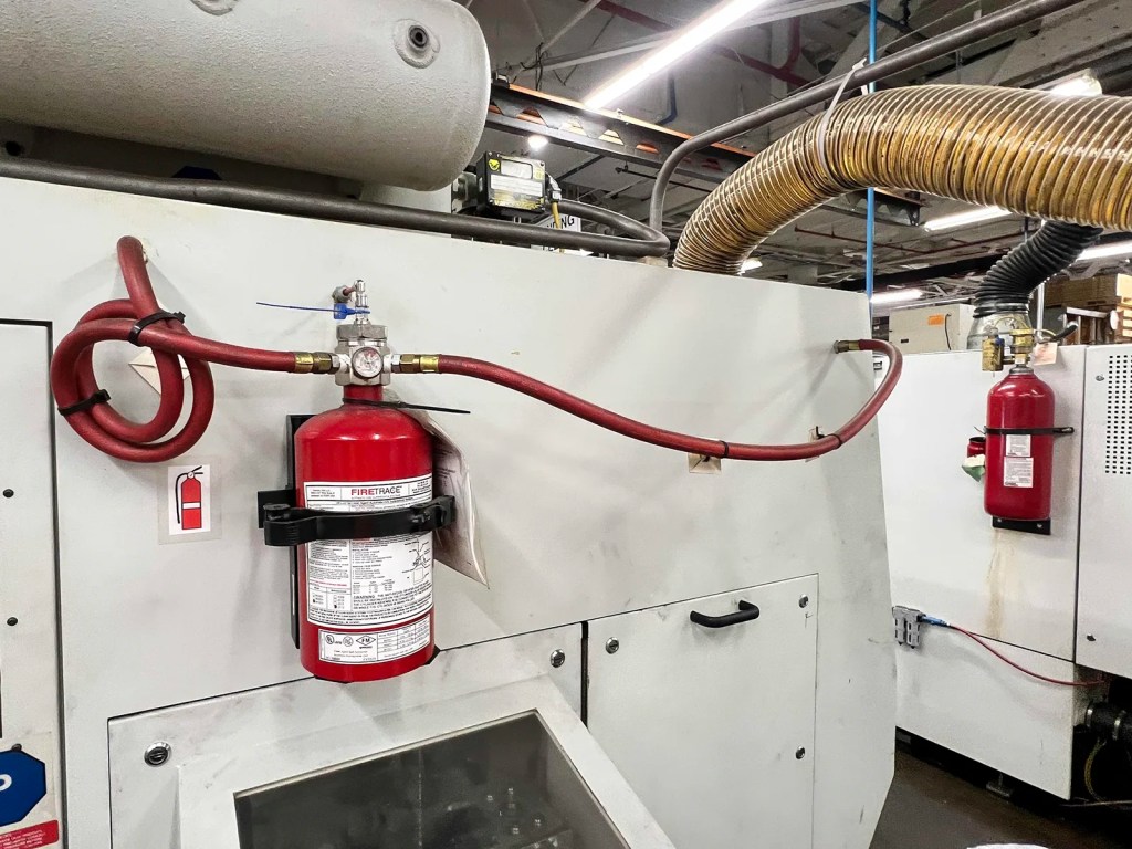 Close-up of a fire suppression system featuring a red fire extinguisher and connecting hoses mounted on industrial machinery.