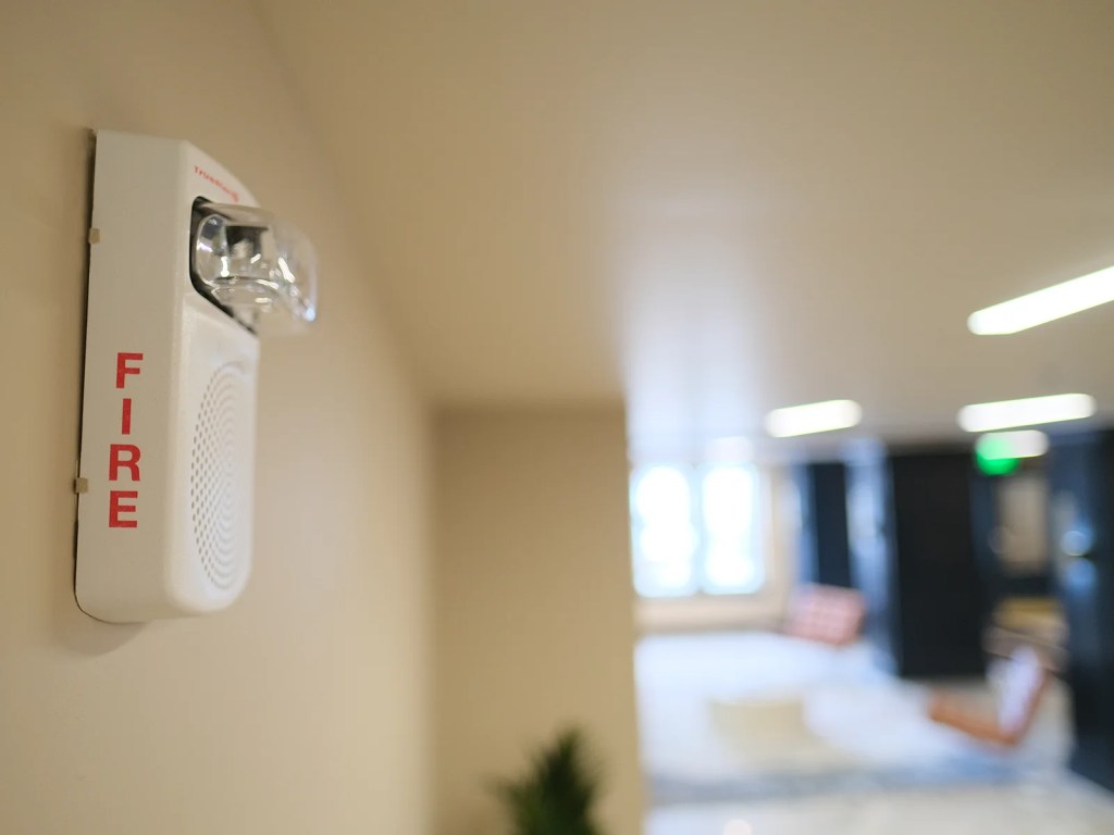 Fire alarm speaker mounted on a wall in a hallway with blurred background decor.