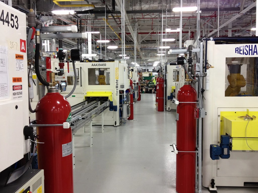 An industrial manufacturing facility featuring multiple machines and production equipment, with red fire extinguishers prominently displayed along the aisle.